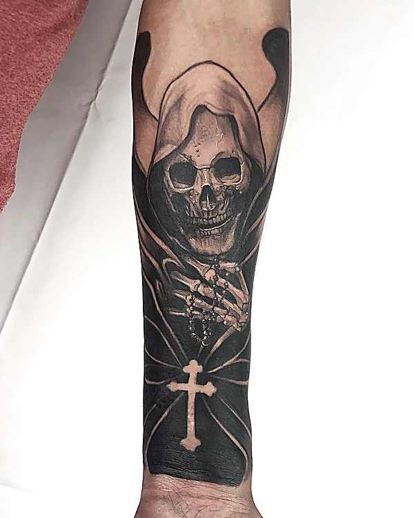 Calavera encapuchada con una cruz, en negro sólido sobre el antebrazo.