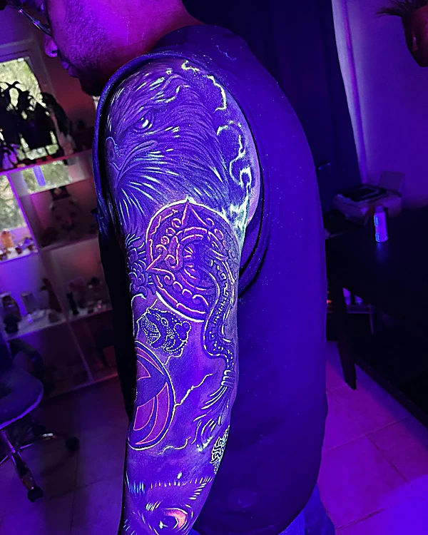 Manga completa en el brazo bajo luz UV, con trazos azules y violetas que brillan sobre la piel.