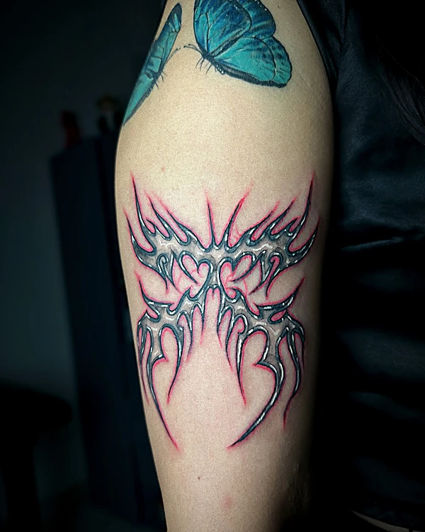 Mariposa de trazo tribal en rosa y turquesa, tatuada en el brazo, con luz normal.